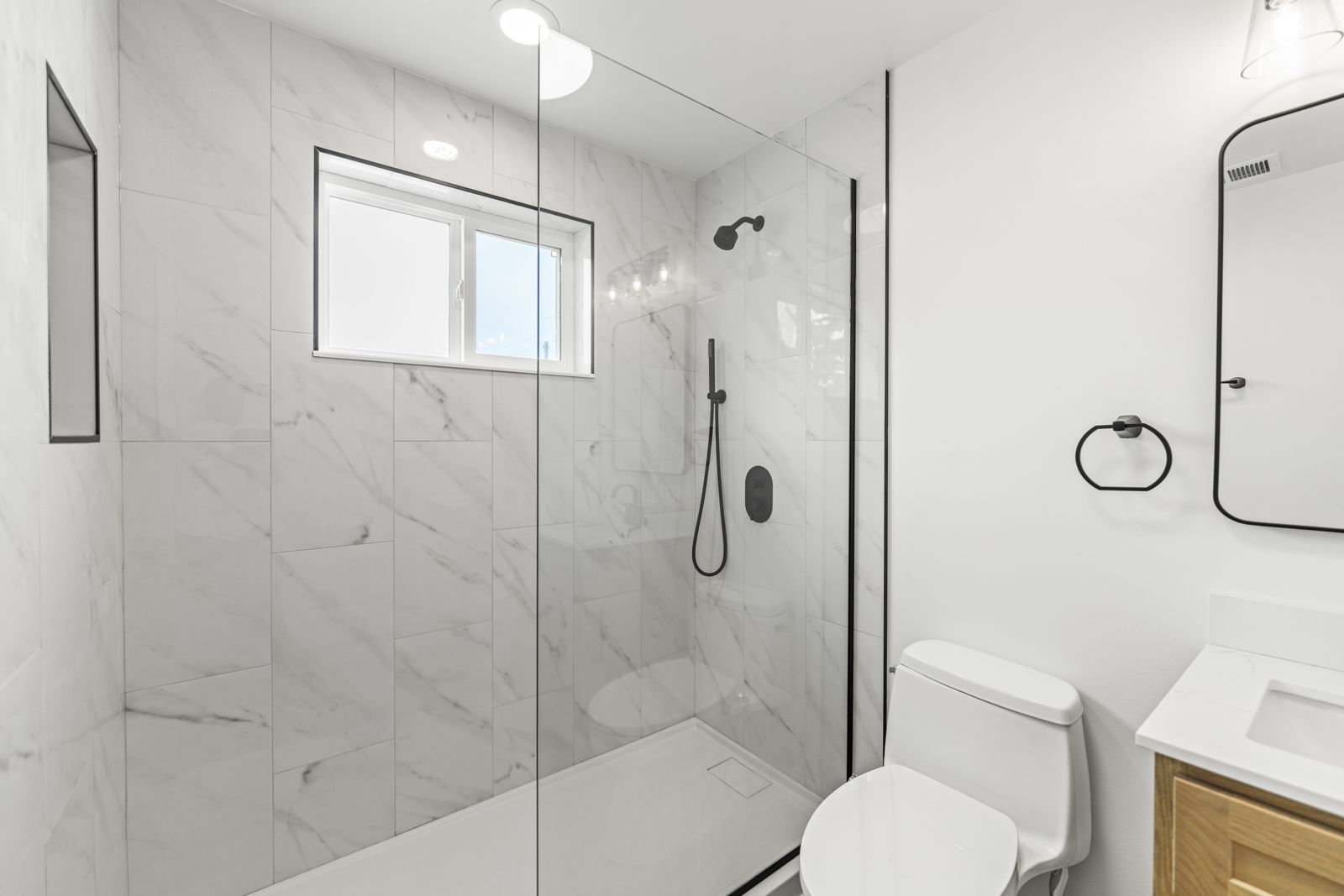 Walk-in shower with marble-look tile, glass panel, and black fixtures